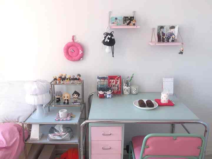 白い壁とピンクの家具が調和した一人用コンパクトなデスクスペース、キャラクターフィギュアとシンプルモダンな装飾が配置されたインテリア