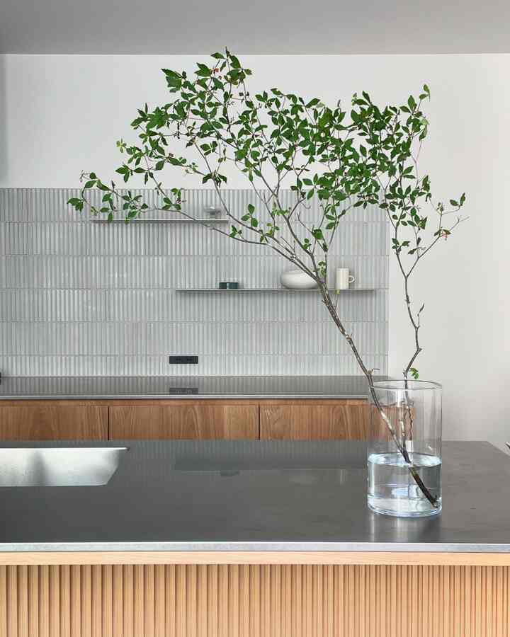 ナチュラルな木目調とステンレス天板が調和したモダンなキッチン、透明な花瓶に活けられた緑の枝が印象的な空間