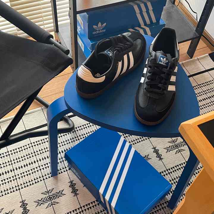 ブルーとブラックのトーンのコンパクトな空間、ブルーのスツールの上に置かれたアディダスのスニーカーと積み重ねられたシューズボックスが配置された清潔感のあるインテリア