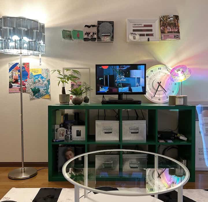 モダンな雰囲気の8畳リビング、中央に透明なガラスのコーヒーテーブル、緑のテレビ台、左側に銀色のフロアランプが配置された居心地の良い空間