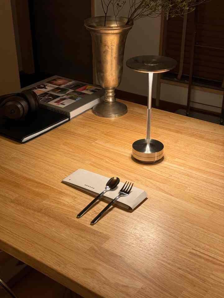 暖かい木目調のテーブルにカトラリーとテーブルランプが置かれた、居心地の良いキッチンのインテリア