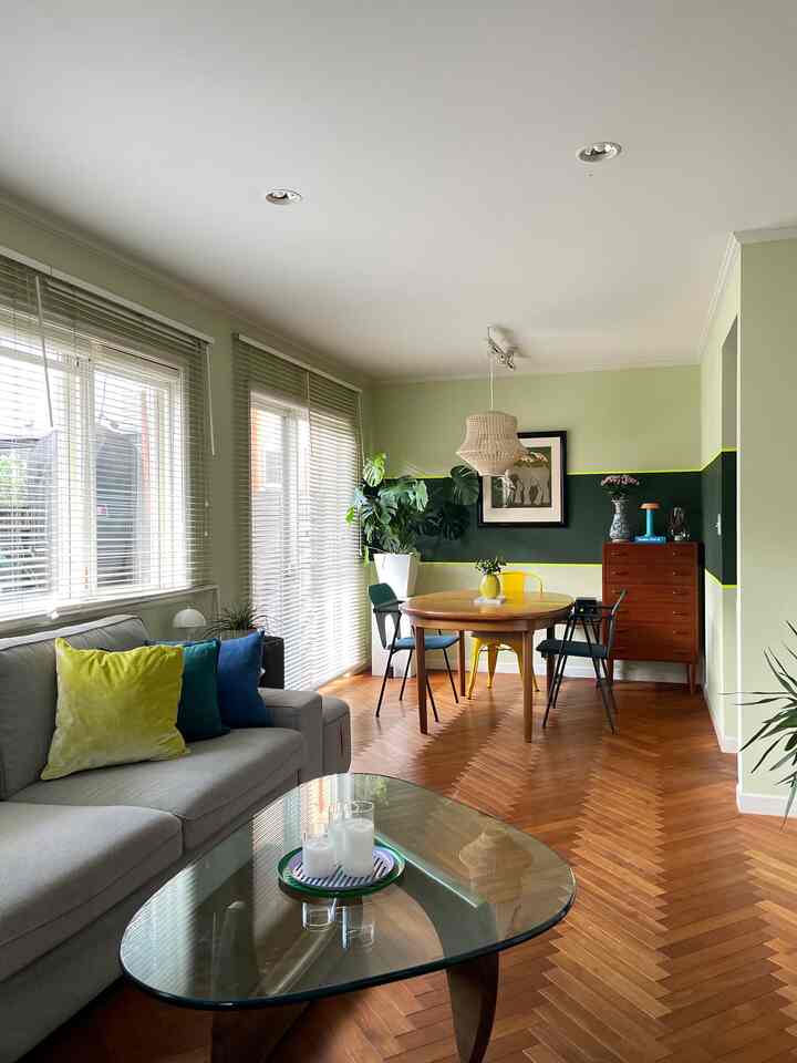 Pastel green toned living room featuring round wooden dining table, gray sofa, and glass coffee table creating cozy atmosphere
