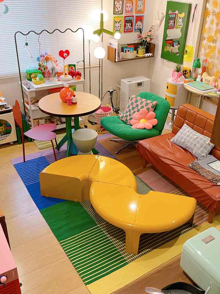 Bright and colorful living room featuring a yellow modular table, orange sofa, and green armchair with retro vibe