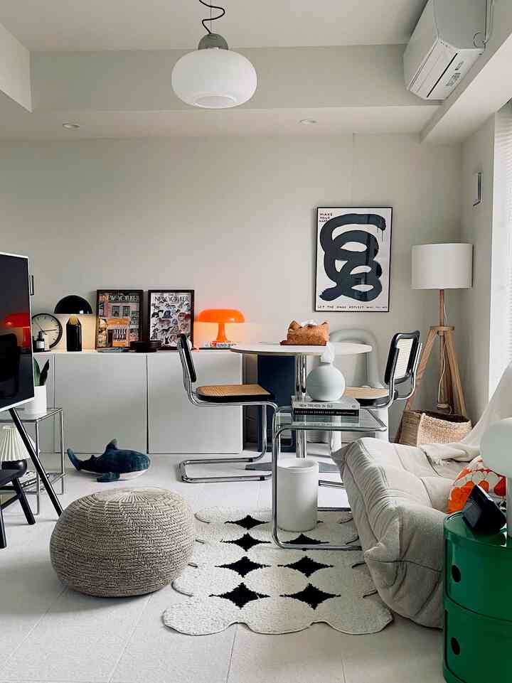 Modern living room with white and beige tones featuring sofa, ottoman, distinctive rug, and various lighting elements