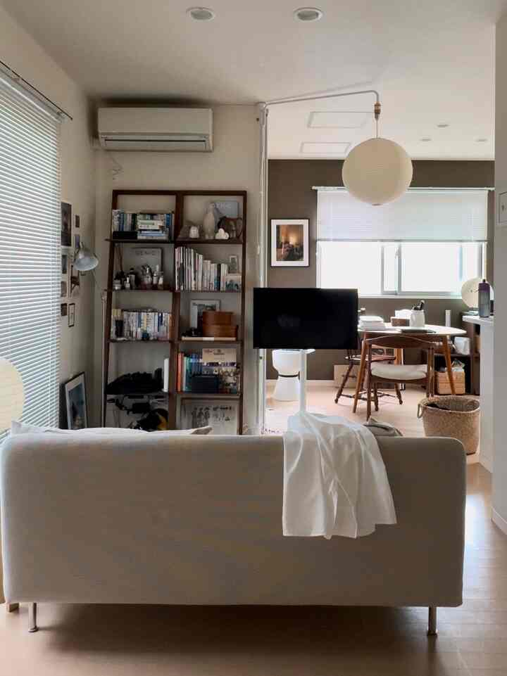 White and brown toned single household living room featuring a sofa, bookshelf, and home office area with a clean and warm atmosphere