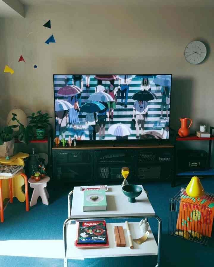 Living room with blue carpet and black TV stand, featuring a colorful mobile and wall clock in a simple modern style