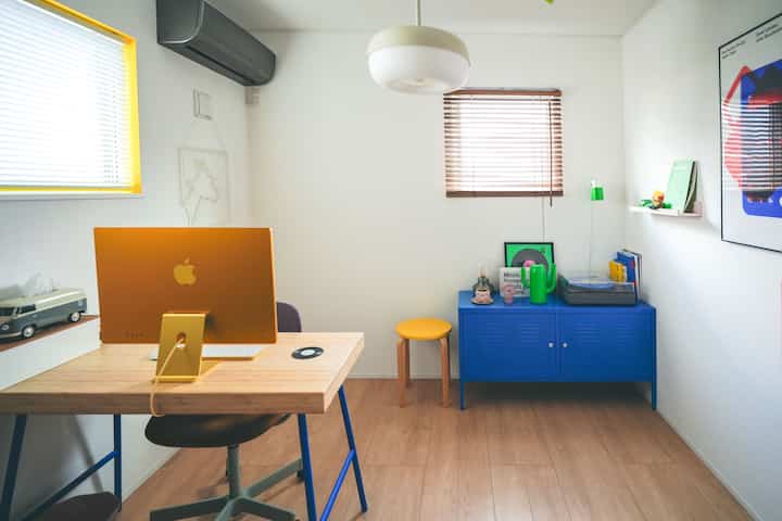 白い壁と木目調の床のワークスペース、黄色と青色の家具が調和するモダンなオフィス空間