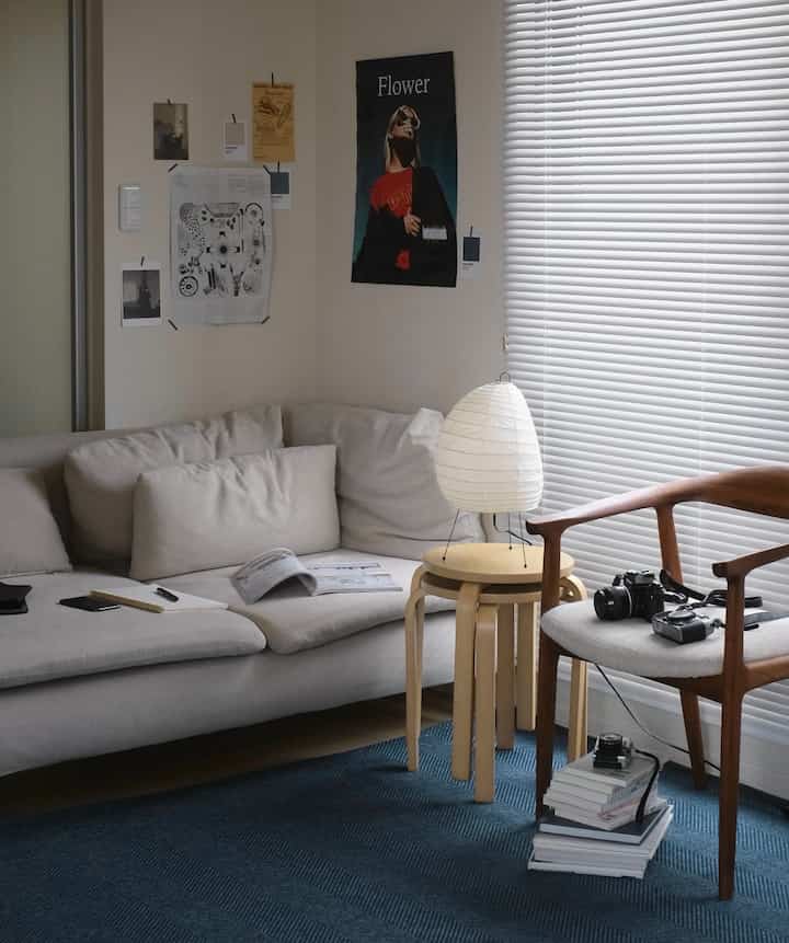 ライトグレーのソファと木製のアームチェア、白いブラインドがあるネイビーカーペットの北欧風リビングルーム