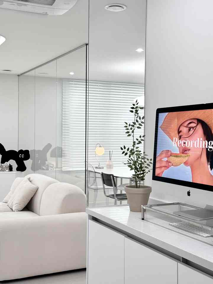 White-toned living room and home office space featuring a large sofa, glass partition, dining table, and desk in a clean modern interior