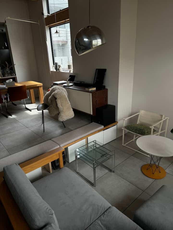 ナチュラルな色調とモダンなデザインが融合したリビング、グレーのソファと丸いコーヒーテーブル、フロアランプが配置された落ち着いた空間