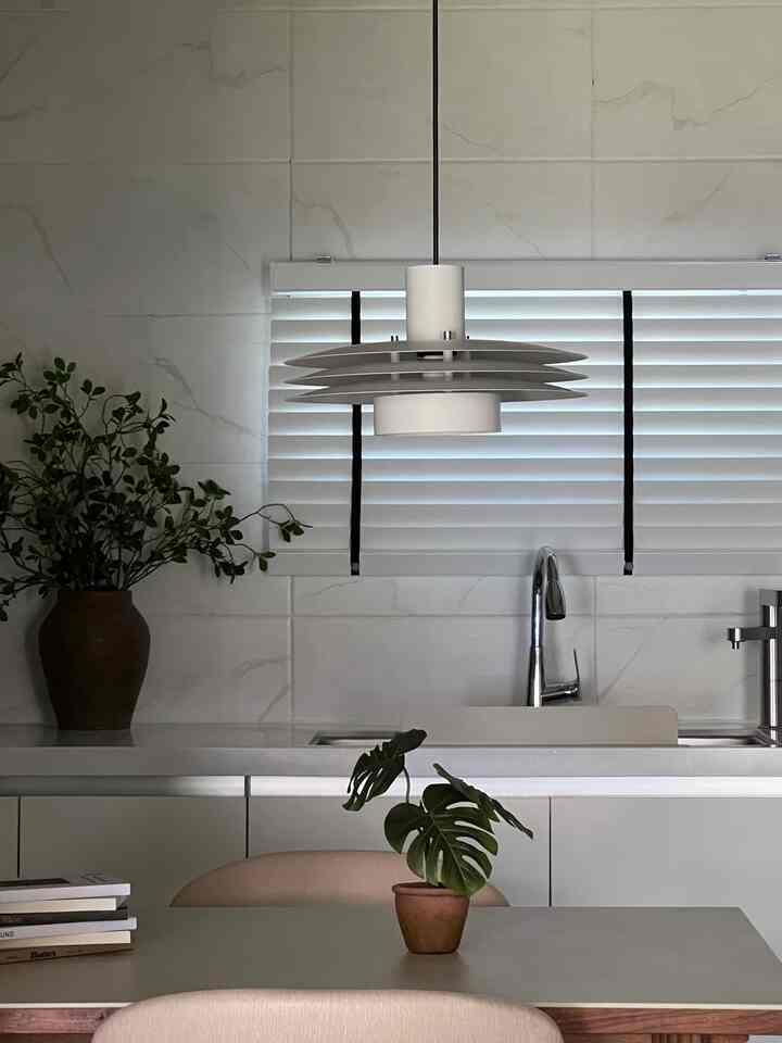 White and green toned kitchen featuring a pendant light, dining table, and plant decor creating a modern and natural atmosphere