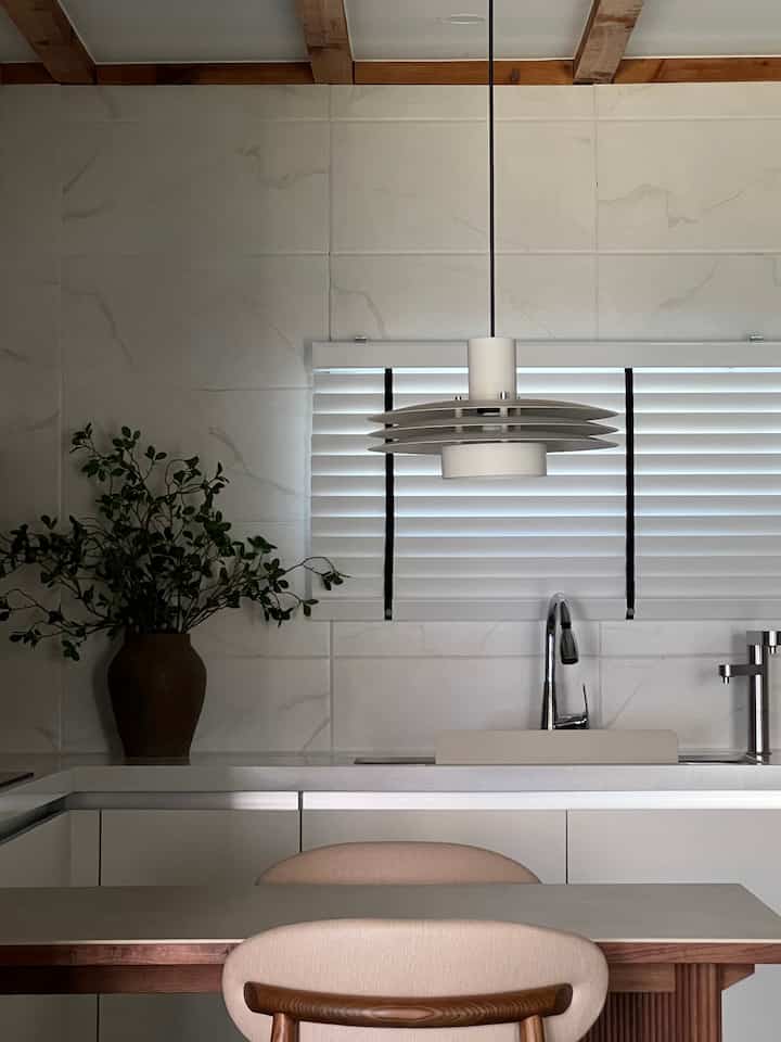 Beige and white toned kitchen space featuring natural wood dining table and pendant light with clean modern interior