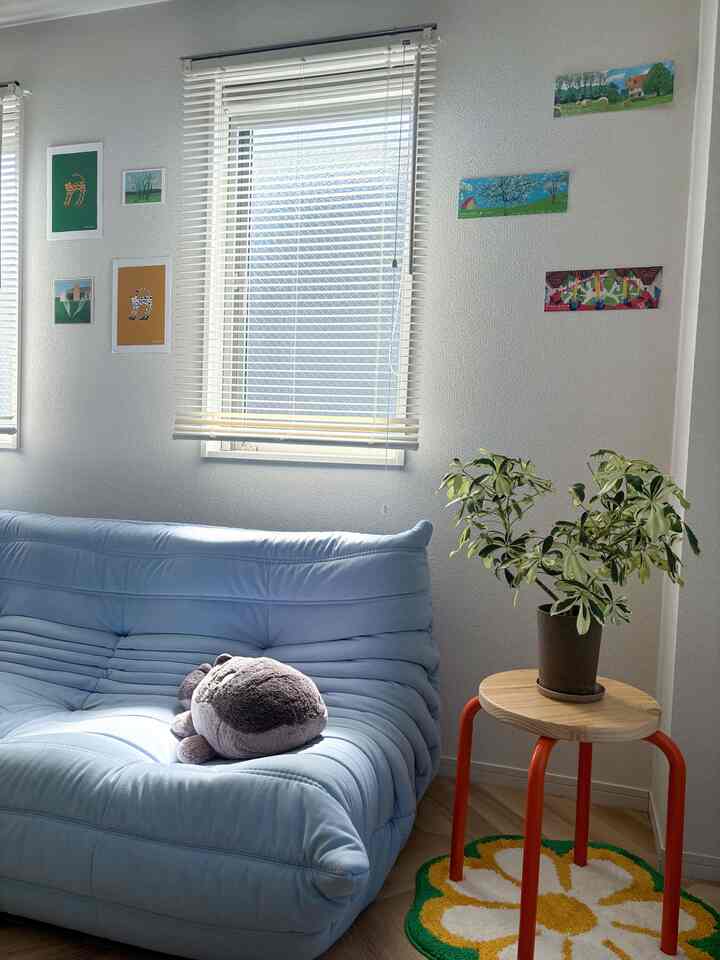 ホワイトとパステルブルー調のリビング、中央の窓とソファ、スツールの上に植物が置かれた雰囲気のある空間