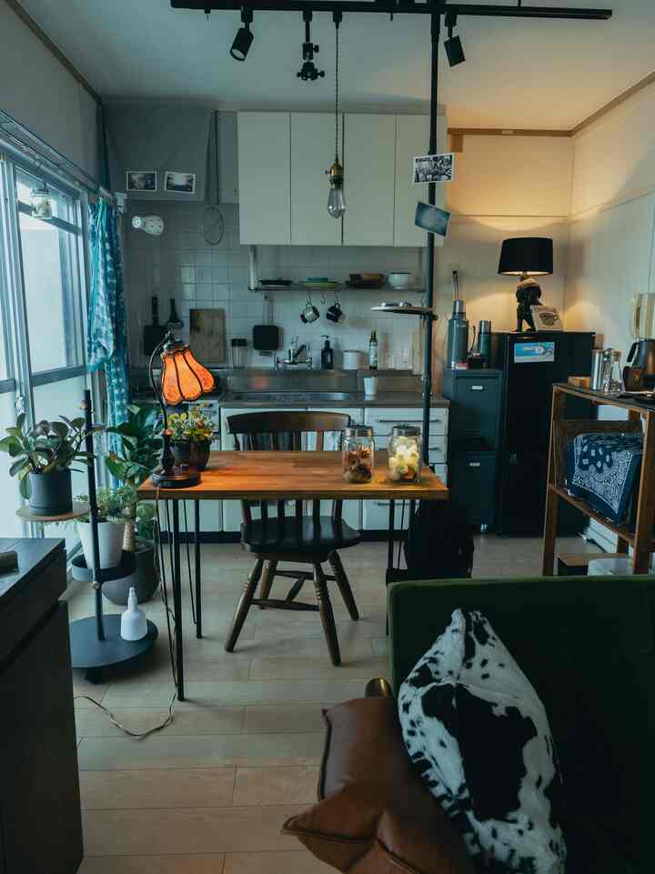 ナチュラルカラーの一人暮らしキッチン、木製のダイニングテーブルとテーブルランプ、植物が配置された雰囲気のあるインテリア