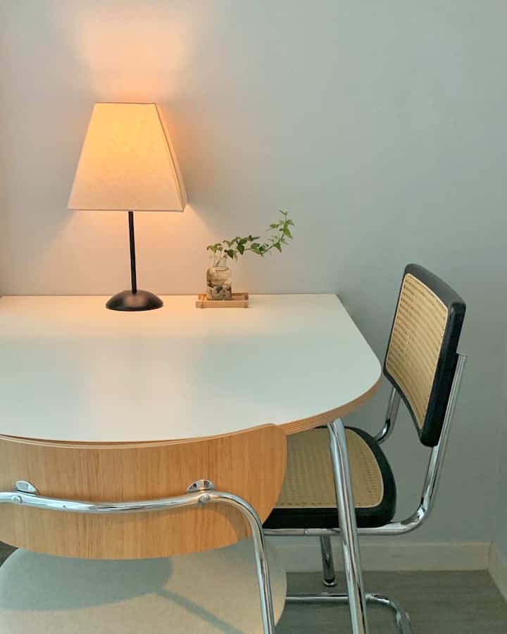 Natural color toned minimal room featuring wood and chrome dining chairs, white table with a table lamp creating a calm atmosphere