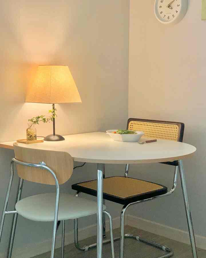 Mid-Century Modern studio apartment dining area with white oval dining table and rattan chairs with chrome frames