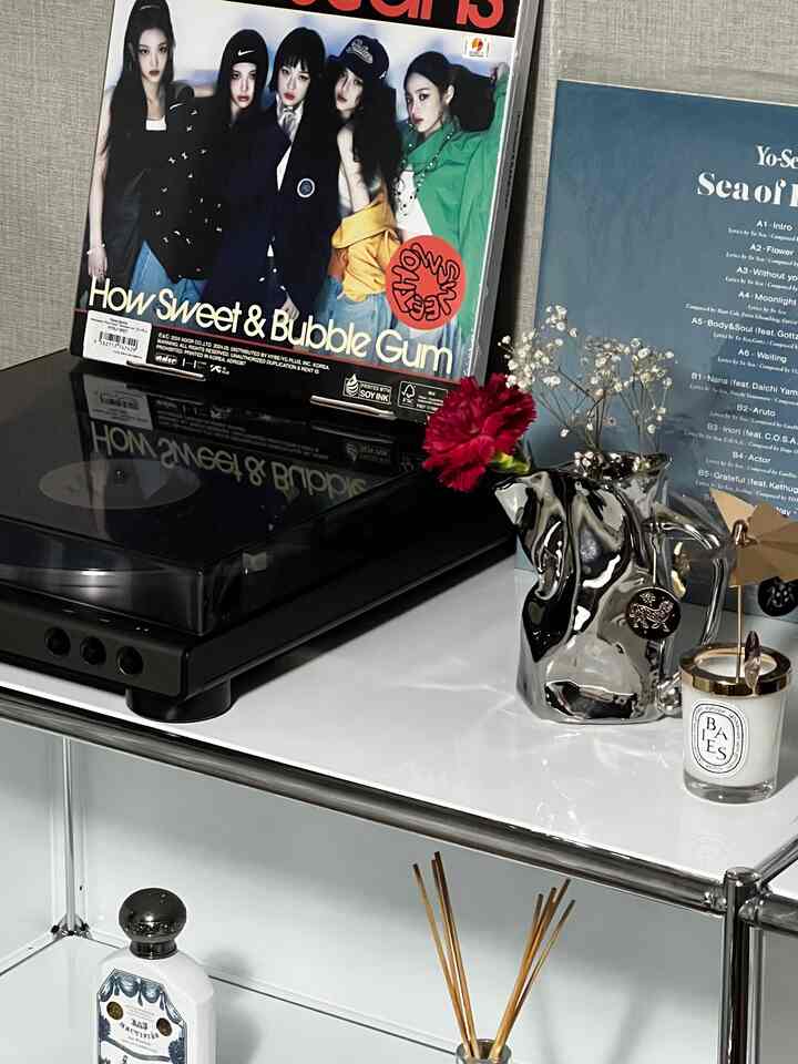 Minimalist and trendy living room with a white table featuring a black turntable, silver vase with flowers, and a candle