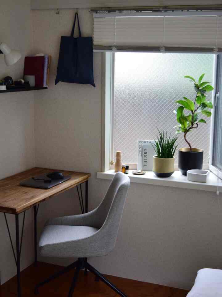ウッドトーンの自然光が差し込むコンパクトな空間に、デスクと回転椅子、窓辺の植物が配置されたナチュラルモダンなホームオフィス
