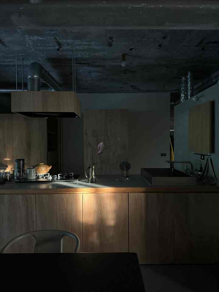 暗いトーンと自然な木材のモダンなキッチン、鏡に夕日の光が反射し温かみのある雰囲気を演出