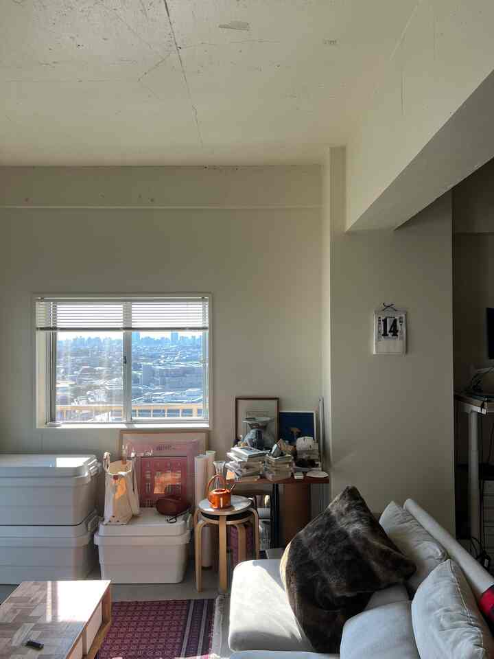 白とナチュラルカラーのワンルームリビング、ソファとスツール、コーヒーテーブルが配置されたシンプルで明るい空間