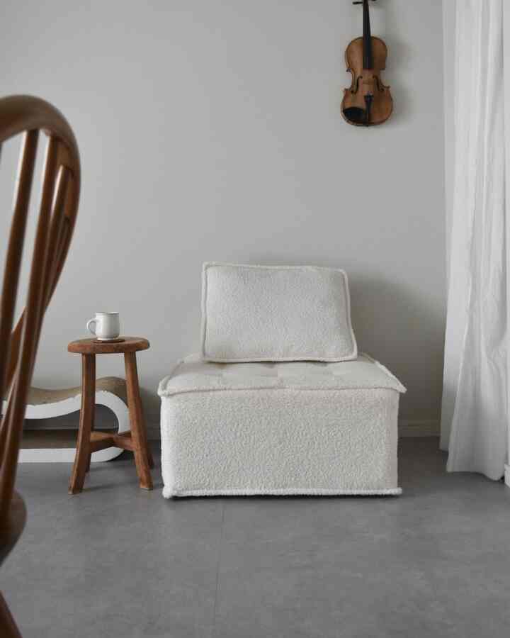 白と茶色のトーンのリビング、シンプルなアームチェアと木製スツールが配置された自然な雰囲気のあるインテリア