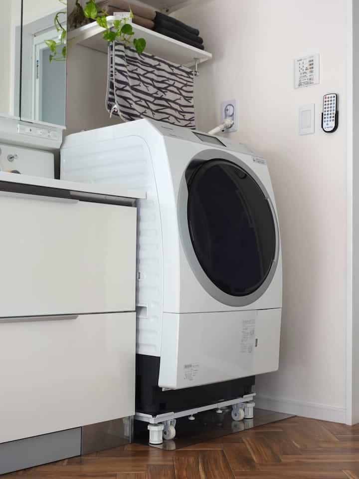 白とナチュラルトーンの洗面所兼ランドリールーム、大小のタオルと壁棚が整然と配置されたモダンな空間