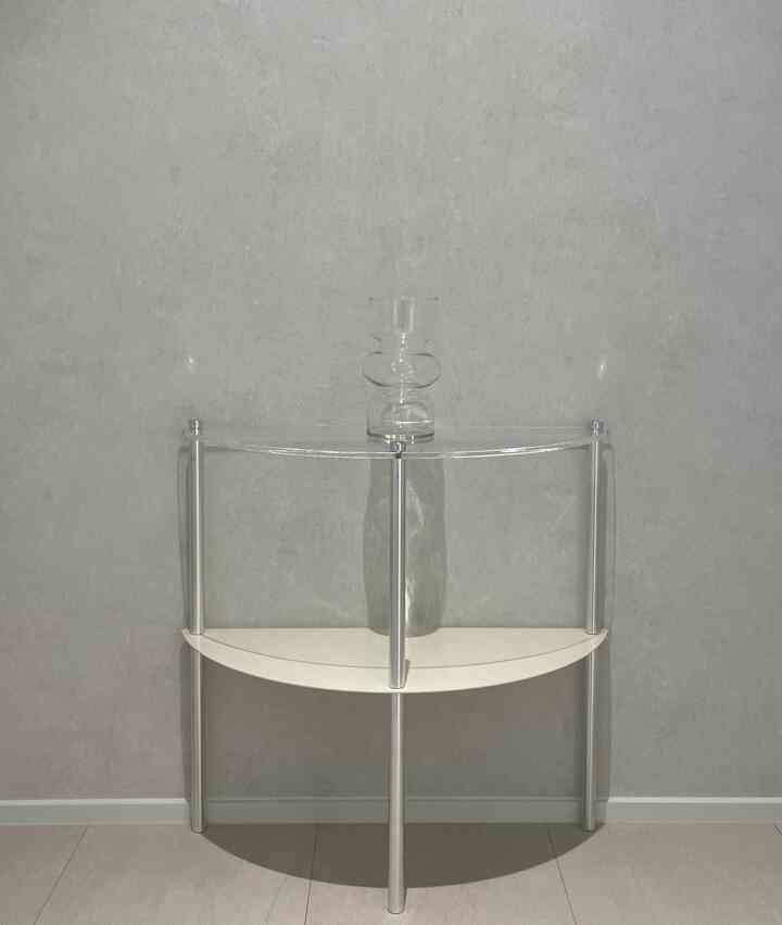 透明アクリルとシルバーのステンレス素材を用いた半円形のナイトテーブルに、中央に置かれたガラスの花瓶があるミニマルでモダンな空間