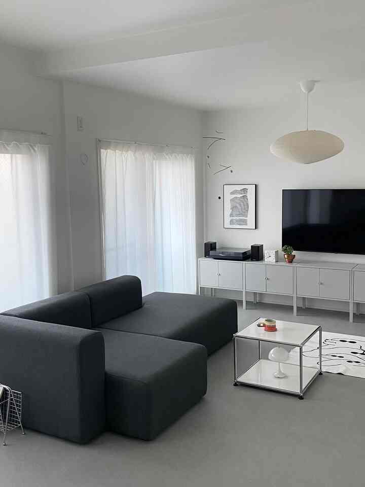 モノトーンのリビングルーム、ダークグレーのソファとホワイトのキャビネット、シンプルなペンダントライトが配された清潔感あるインテリア