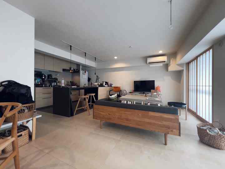 白と木目調のリビングとキッチン、ナチュラルモダンなソファとスツールが配置された雰囲気の良い空間