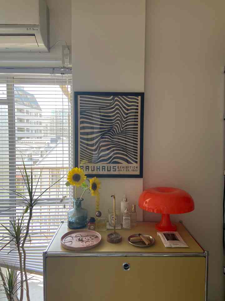 イエローのキャビネットとレッドのテーブルランプが置かれたミッドセンチュリーモダンなリビングの一角、黄色いひまわりと花瓶がアクセントの温かみのある空間