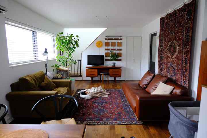 ブラウンとホワイトの色調のリビング、2つのソファと大きなラグが配置され、中央に子供が寝ている自然な雰囲気のインテリア