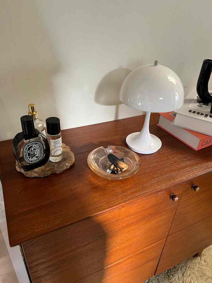 Natural wood tone cabinet topped with table lamp and perfumes creating a cozy setting