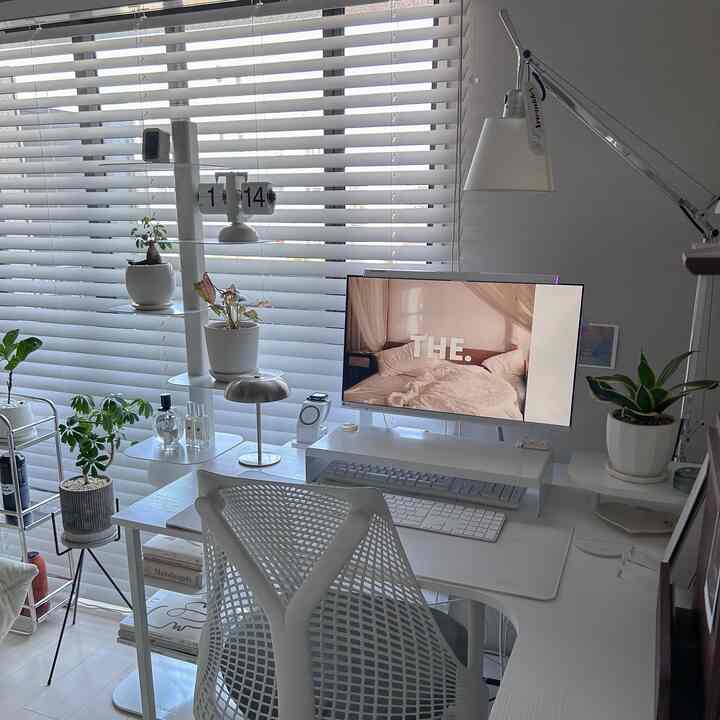 ホワイトトーンのホームオフィス、ホワイトのデスクとチェア、モニターや複数の植物が配された雰囲気の良いインテリア