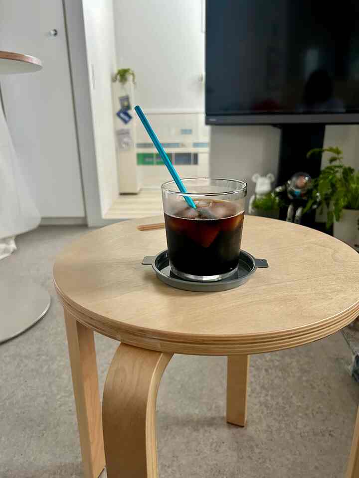 ナチュラルな木目調スツールに置かれたアイスコーヒーと青いステンレスストローが印象的なシンプルでモダンなワンルームの雰囲気あるインテリア