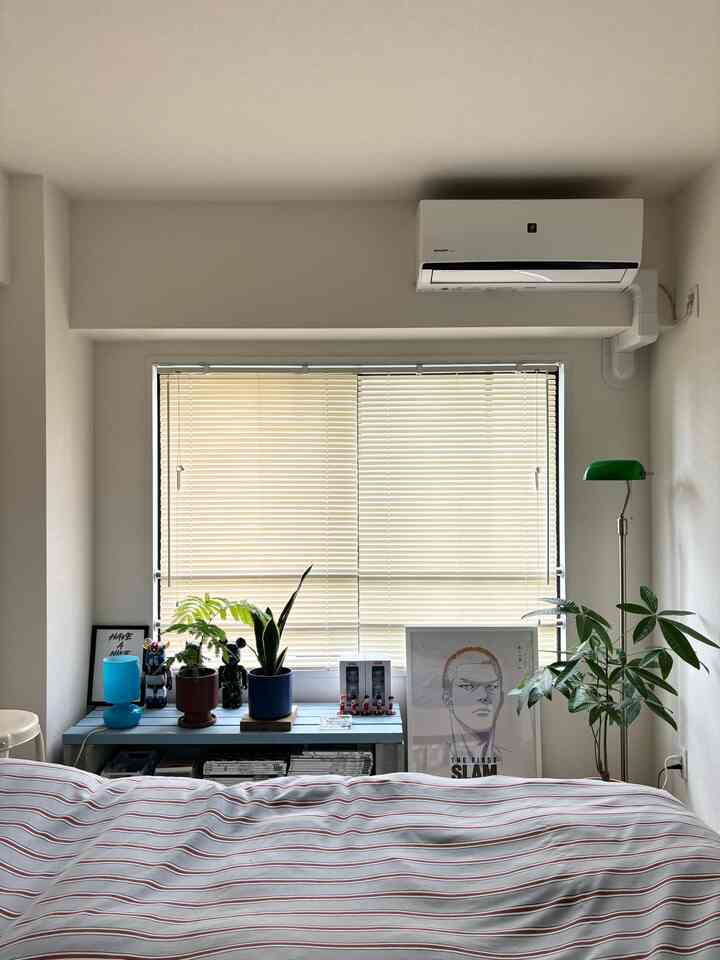 Clean white bedroom with beige blinds closed, featuring plants and decor creating a modern atmosphere