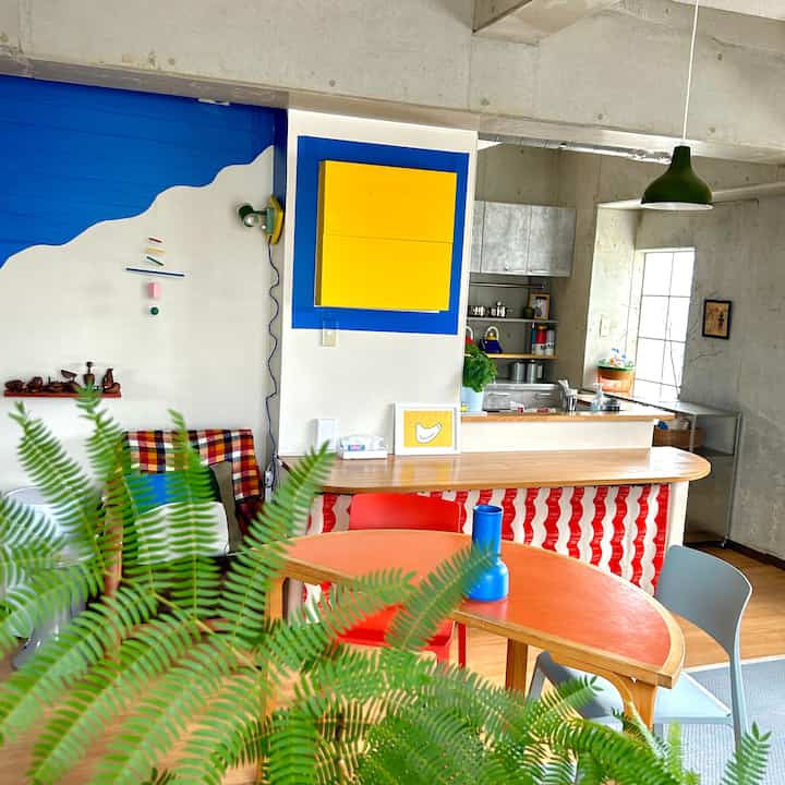 明るい色調のカフェ風ダイニングルーム、半円形のオレンジ色テーブルとカラフルな椅子、自然な植物と木製家具が配置された雰囲気のある空間