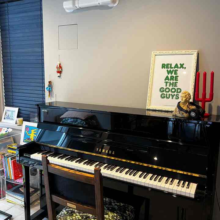 グレーの壁と黒いヤマハのピアノが配置された玄関近くの空間、アンティークチェアとモーツァルトキャンドルで彩られた音楽室の雰囲気あるインテリア