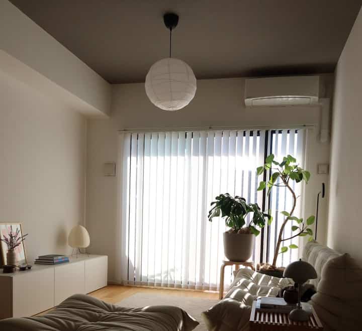 White and natural tone living room featuring large window with plants and stool, creating a cozy atmosphere
