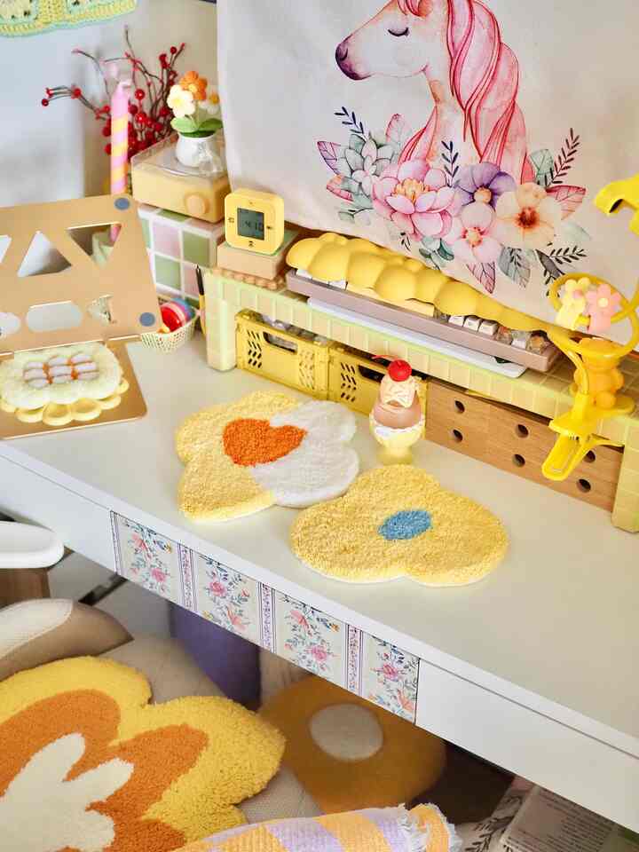 黄色と白のトーンの子供部屋のデスクスペース、花の形のラグとユニコーンのポスターが配置された可愛らしいインテリア