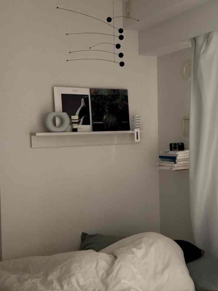 ホワイトとナチュラルトーンの寝室、遮光カーテンと壁掛け棚が配置された落ち着いた雰囲気のインテリア