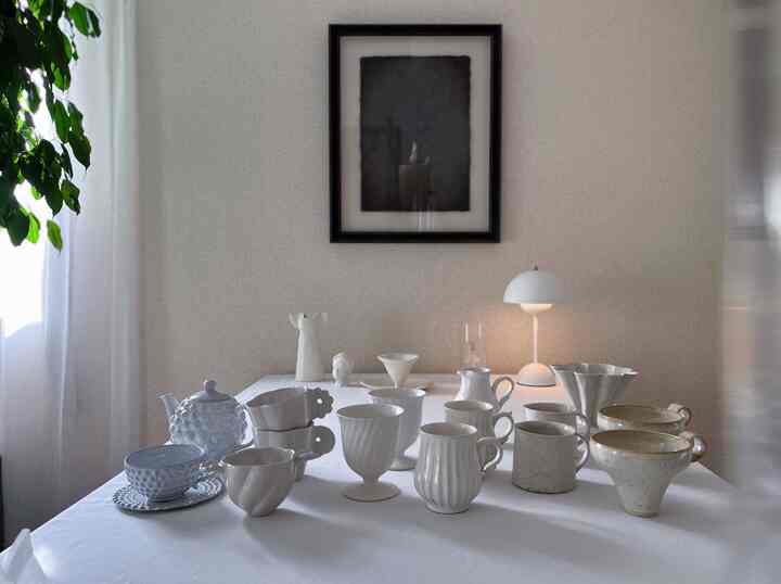 White-toned kitchen table featuring various white tableware arranged neatly in a simple setting