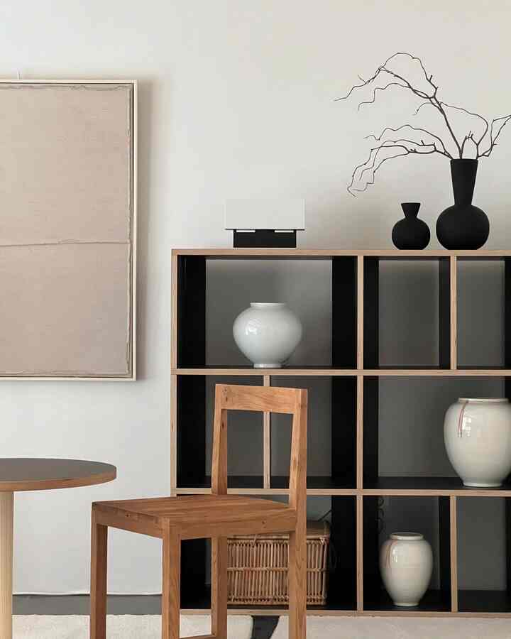 明るい木目調と黒色のリビング、シンプルな椅子と黒い棚に白い陶器のオブジェが配置されたモダンでナチュラルな空間