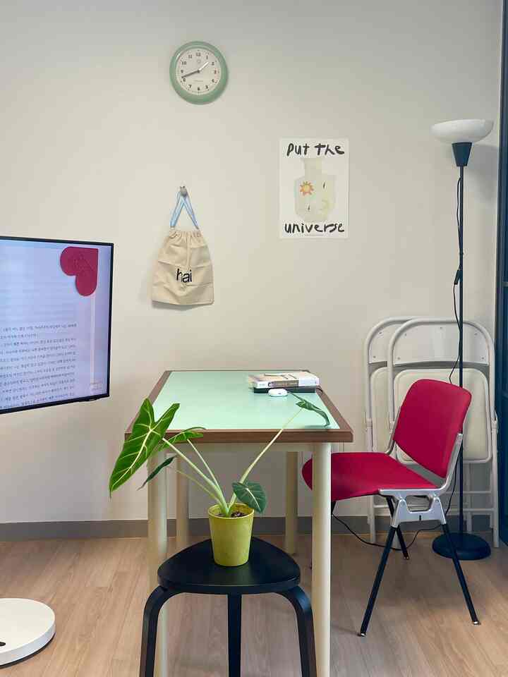 白い壁とミント色のダイニングテーブルがあるワンルーム、ピンクの椅子と植物がシンプルでコンパクトな雰囲気を演出