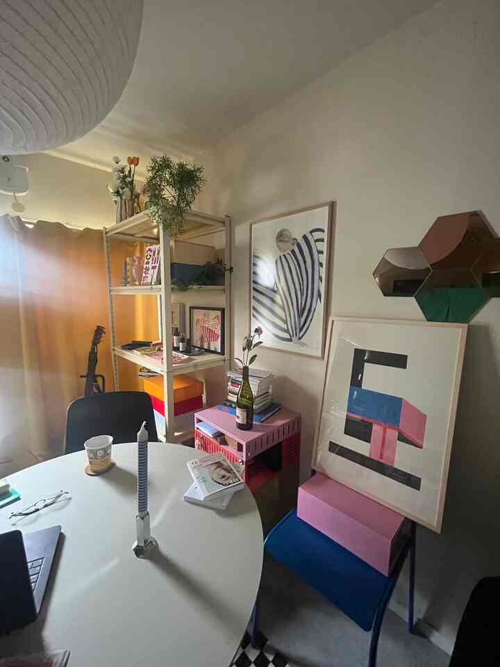 ホワイトとベージュの色調のダイニングルーム、丸テーブル、棚、ポスターと壁の鏡が配置された雰囲気のあるインテリア