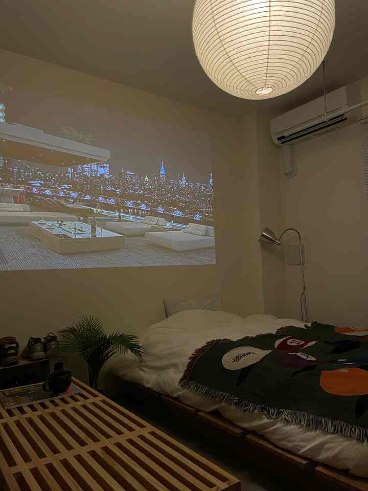 Natural tone simple bedroom featuring a cozy bed, pendant light, and large projector screen on the wall creating a comfortable space