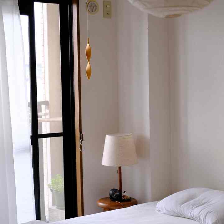 白とナチュラルカラーの寝室、木製のナイトスタンドとテーブルランプが配置された落ち着いた雰囲気のインテリア