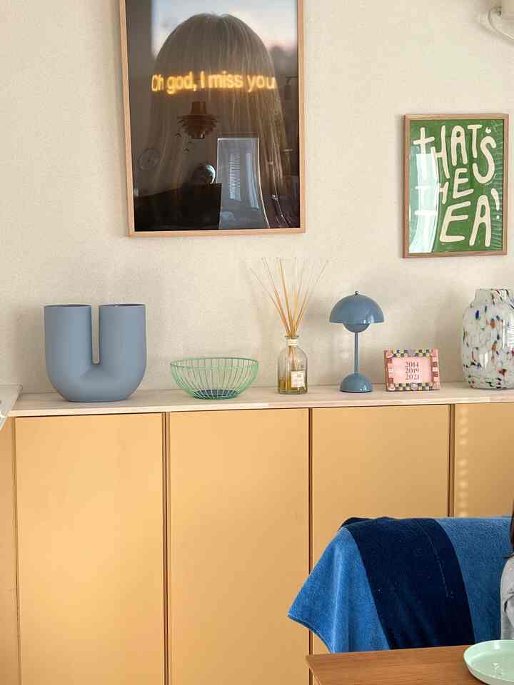 ベージュのチェストにブルーのランプや花瓶が置かれた、シンプルでナチュラルな雰囲気のリビングの壁面