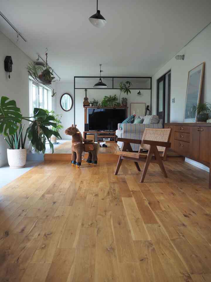Bright spacious living room with natural wood-tone flooring and plants, featuring a sofa and sideboard along walls