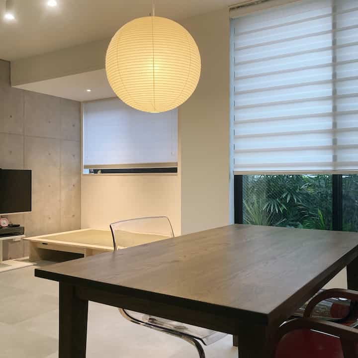 ベージュとホワイトの色調のダイニングルーム、木製のダイニングテーブルと透明な椅子、畳ベッドが配置された自然でモダンな雰囲気のあるインテリア。