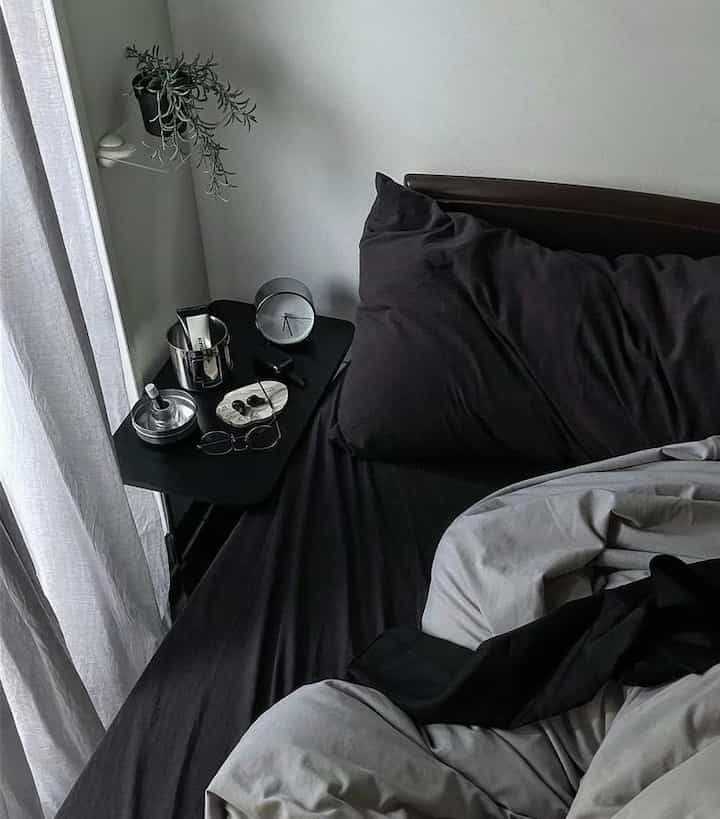 グレーのトーンの寝室、黒いベッドリネンとシルバーの小物が配置されたシンプルなナイトテーブルのある雰囲気のあるインテリア